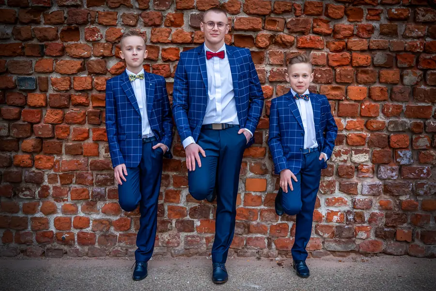 Dwóch chłopców i młody mężczyzna w garniturach w niebieską kratę przy ceglanym murze