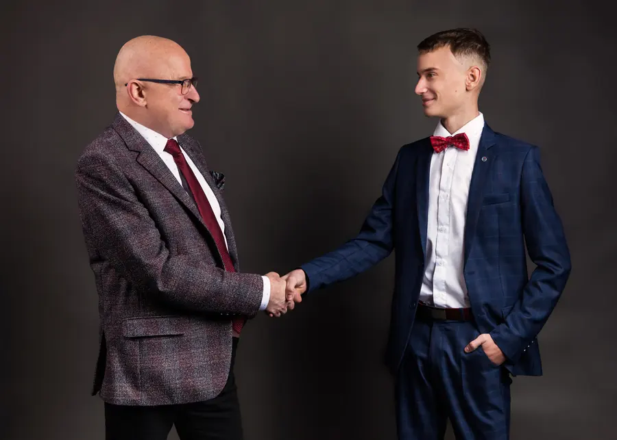 Starszy i młodszy mężczyzna w garniturach ALJEKA podają sobie ręce